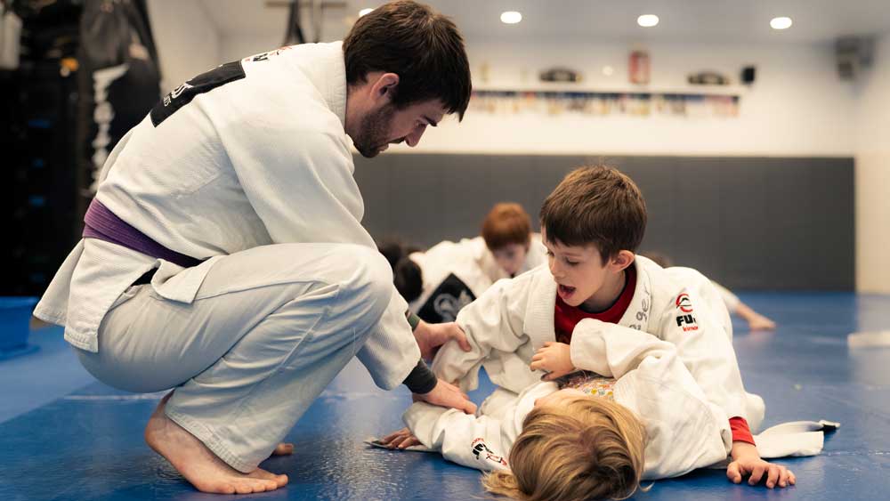 A martial arts instructor guiding two small kids as they fight in the floor