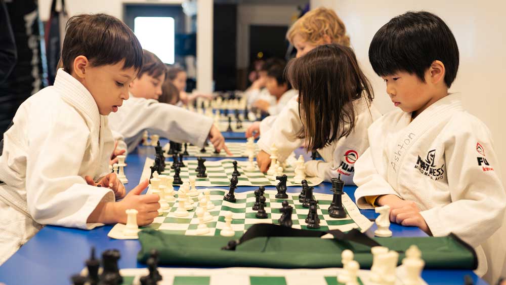 Two kids playing chess and wearing karate suits