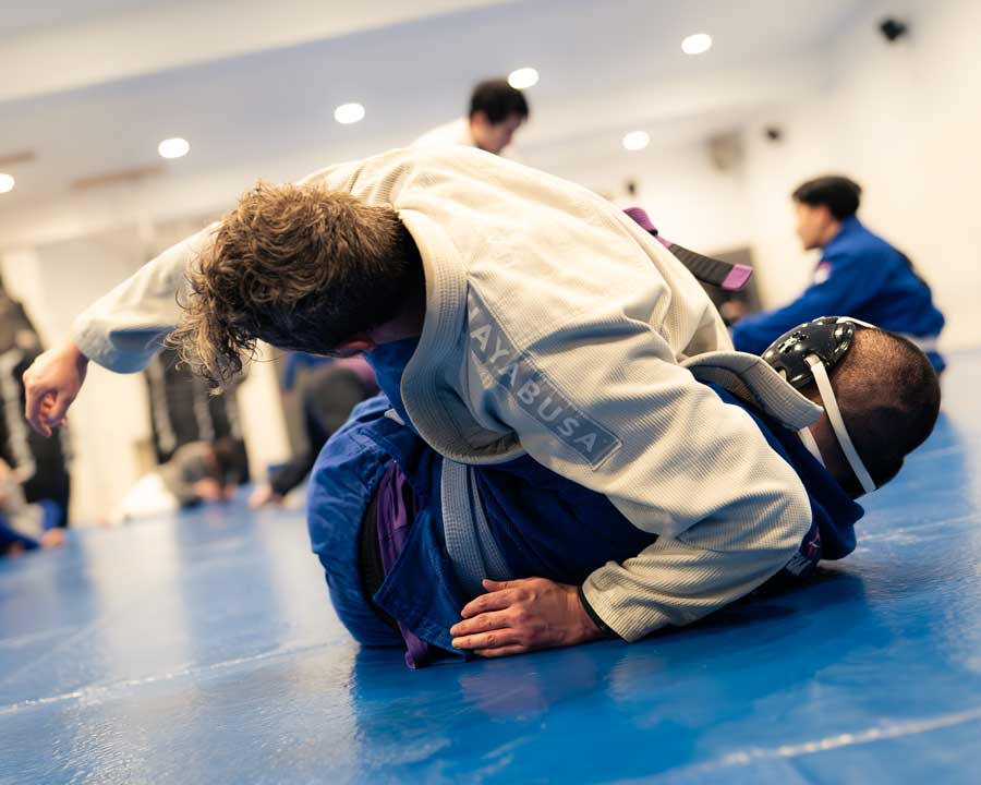 Two people wrestling on a mat, one wearing a white gi and the other in blue