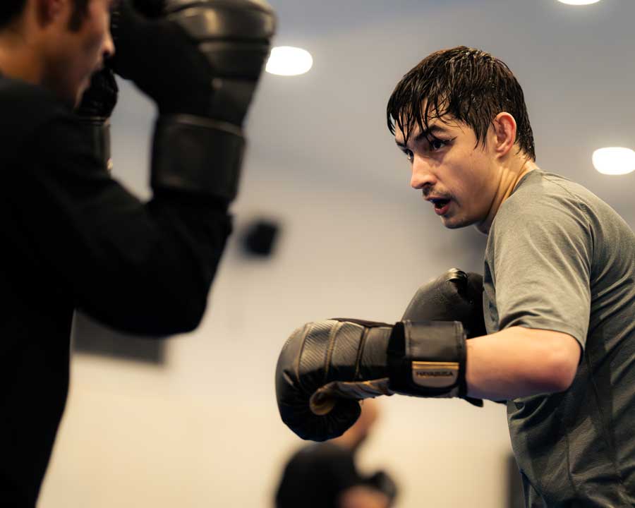 Two guys boxing in a gym, both wearing black gloves