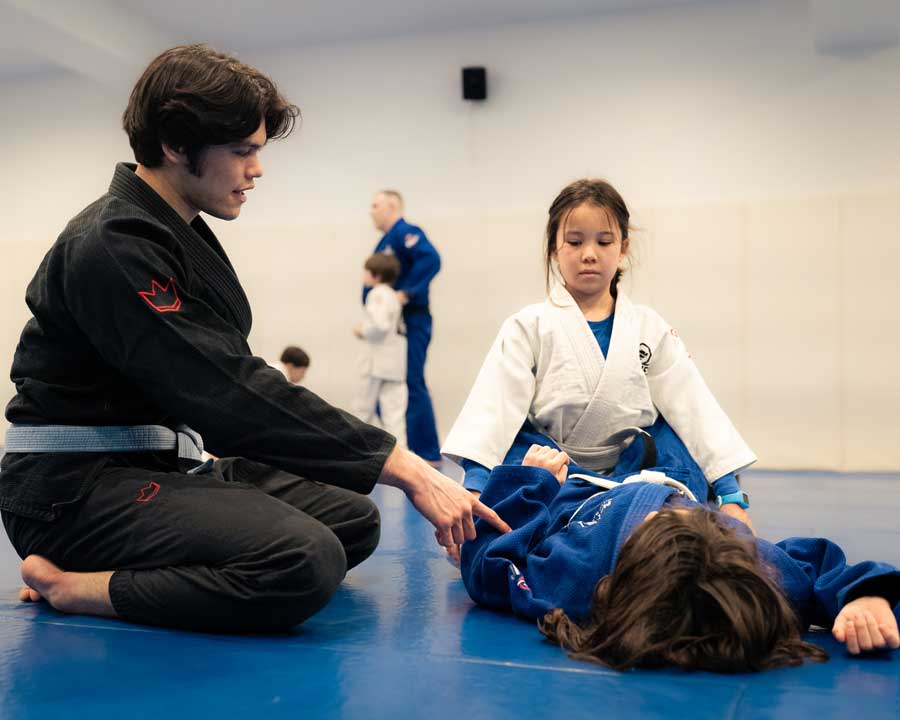 Instructor showing two kids a move on the mat during a judo class