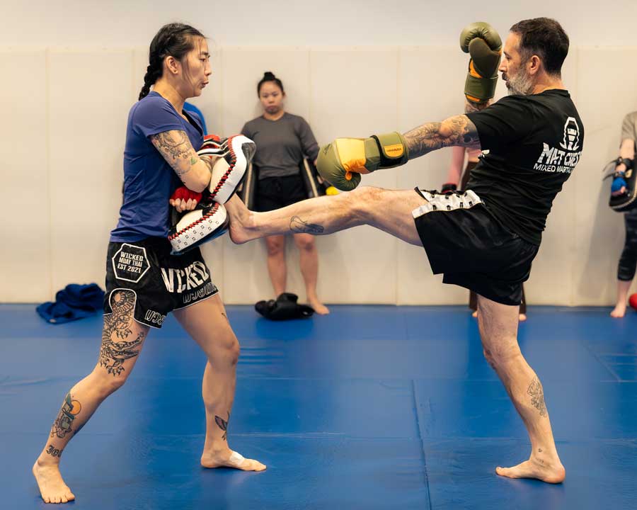 Man kicks a pad held by a woman during a martial arts training session