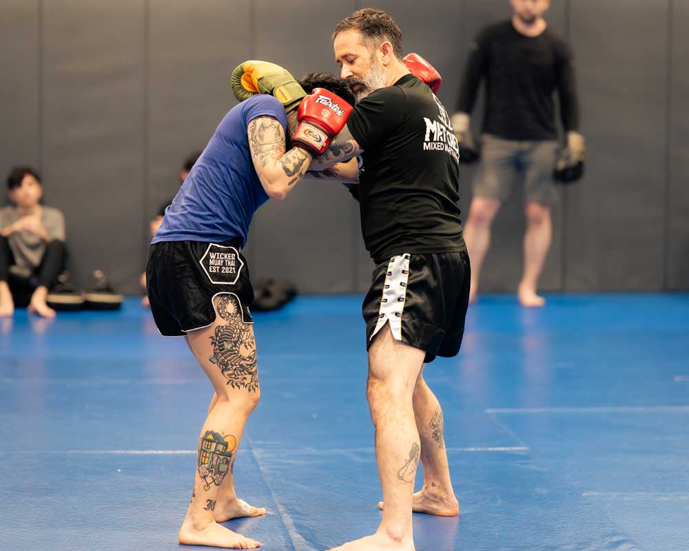 Man and woman practicing with boxing gloves in a martial arts class, other people in the background