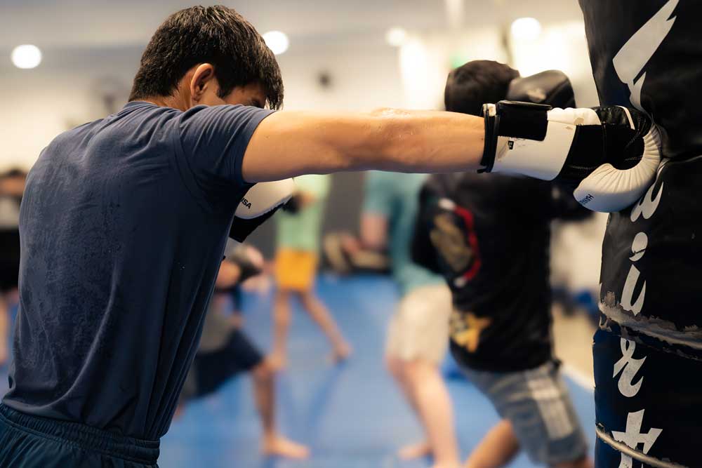 Guy in boxing gloves punching a heavy bag in a busy gym