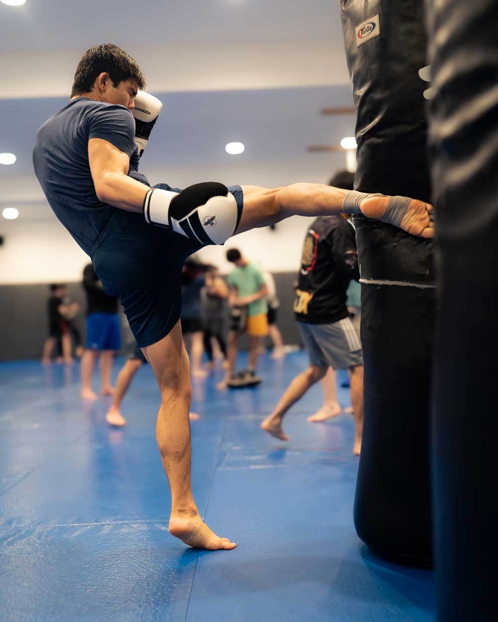 Guy throwing a high kick at a punching bag in the gym