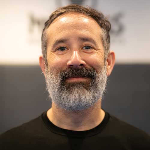 Man with a full gray beard smiling, wearing a black shirt